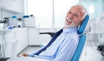 Older man in collared shirt and tie smiling in the dental chair