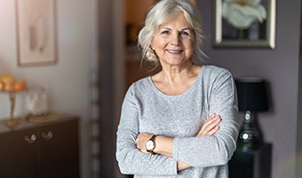 Older woman in grey shirt smiling while crossing her arms