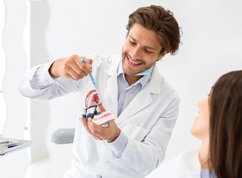 A dentist using a mouth mold to show a female patient how a dental bridge works