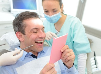 A male patient looking at his new and improved smile, complete with a dental crown and bridge fixture in place