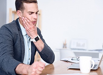 Man sitting at desk at work and rubbing jaw