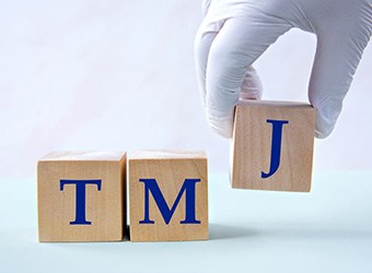 Gloved hand placing wooden blocks that read “TMJ”