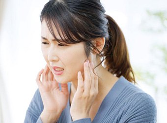 Woman grimacing as she experiences symptoms of TMJ disorder