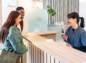 Dental receptionist smiling at couple in lobby