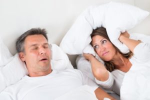 woman covering ears pillow husband snoring