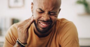 Man wincing in pain and holding side of face. 